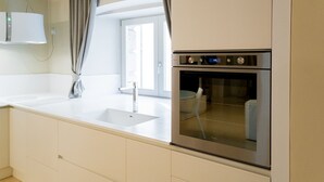 Una cocina moderna con horno empotrado, lavamanos y ventana con cortinas.