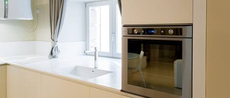 A modern kitchen with a built-in oven, a sink, and a window with curtains.