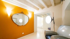Un pasillo con un espejo grande en una pared naranja, una lámpara redonda en la pared y una silla moderna.