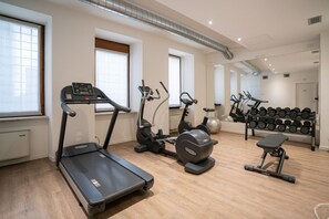 Ein Heimfitnessraum mit Laufband, Crosstrainer, Hometrainer und einer Bank. Auf Regalen befinden sich Hanteln und eine Kettlebell.