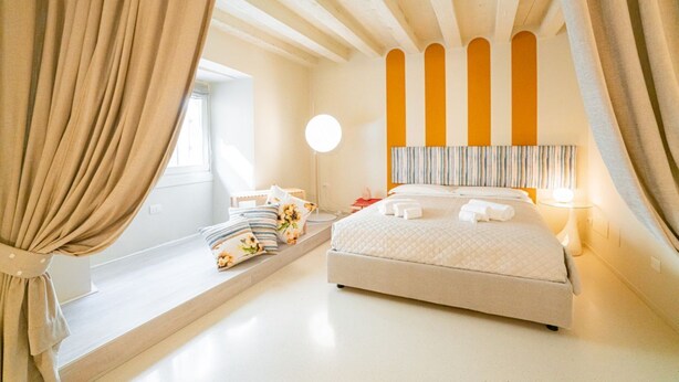 Une chambre à coucher avec un lit, des rideaux, une table de chevet, une lampe et une fenêtre.