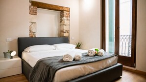 Un dormitorio con una cama, una mesita de noche, una planta en maceta y vistas al balcón exterior.
