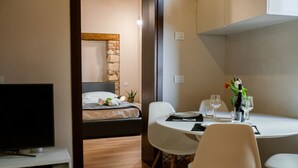 Una habitación de hotel moderna con una cama, un televisor, una mesa de comedor con sillas y una pequeña zona de comedor con un florero.