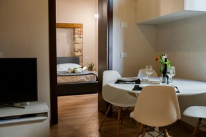 A modern hotel room with a bed, a television, a dining table with chairs, and a small dining area with a vase of flowers. - Modern and comfortable house 30 meters from the Arena (Verona)