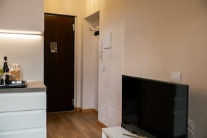 A hotel room with a wooden floor, a white dresser, a flat-screen TV, and a door leading to another room. - Modern and comfortable house 30 meters from the Arena (Verona)