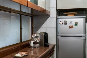 Una cocina con cafetera, tetera, tazas y un refrigerador con imanes.