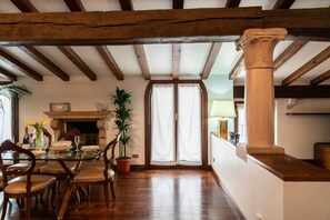A dining area with a glass table, wooden chairs, a fireplace, and a large window with curtains.