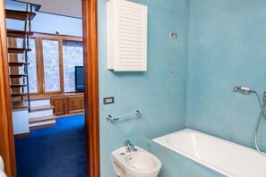 Ein Badezimmer mit einer Badewanne, einem Bidet und einem Fenster mit Blick auf eine Holztreppe und einen Fernseher.
