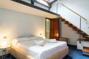 Ein Hotelzimmer mit einem Bett, einem Nachttisch, einer Schreibtischlampe, einer Holztreppe und einer Tür zu einem anderen Raum.