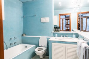 A bathroom with a bathtub, toilet, and sink, with a blue wall and wooden door frames.