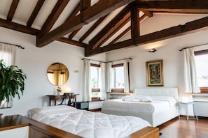 A bedroom with two beds, wooden beams, a round mirror, a painting, and a potted plant.