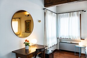 Una habitación con un espejo redondo, una mesita con una lámpara, una silla y una ventana con cortinas.