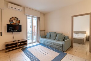 Un salon moderne avec un canapé, un téléviseur, une horloge et une porte-fenêtre coulissante donnant sur l’extérieur.