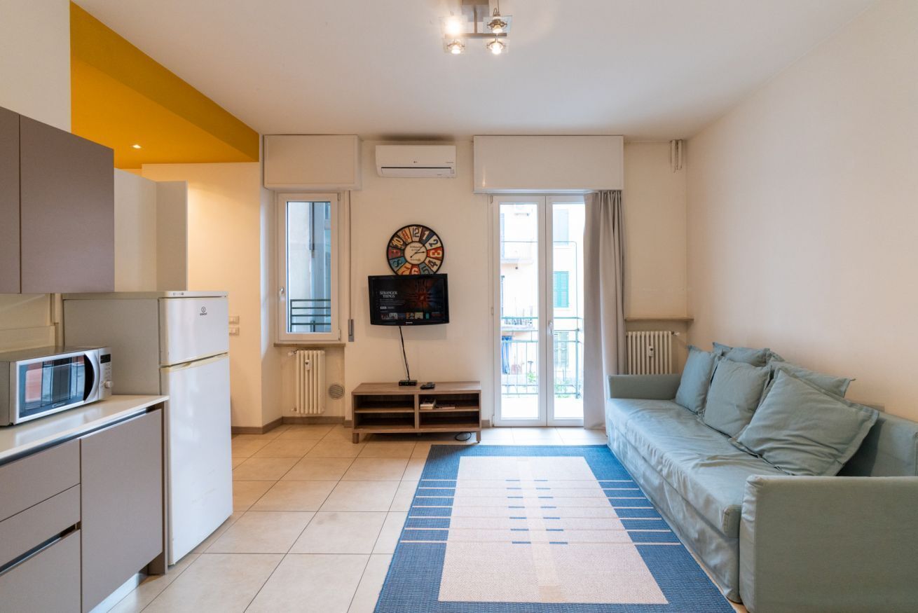 Un ambiente compatto con angolo cottura, televisione a schermo piatto, divano e tappeto decorato.