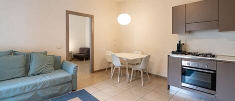 Un espacio habitable compacto con sofá, mesa de comedor, sillas, cocina con horno y una lámpara colgante.