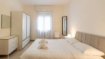 Una camera da letto con un letto, una cassettiera, uno specchio, una sedia e una finestra con tende.