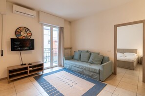 A modern living room with a sofa, a TV, a clock, and a sliding glass door to the outside.