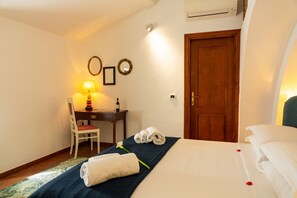 A hotel room with a bed, a desk with a chair, a lamp, and a door. - Magnificent Residence overlooking Piazza Erbe (Verona)