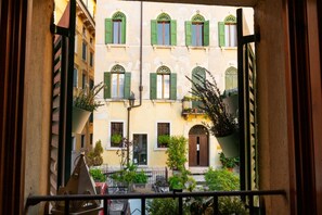 A view from a balcony overlooking a building with multiple windows and balconies, some with plants.