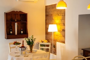 A dining area with a table set for two, a wooden wine rack above, and a wall-mounted lamp.