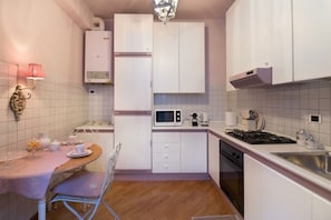 Una cocina compacta con armarios blancos, microondas, estufa y comedor con mesa y sillas.