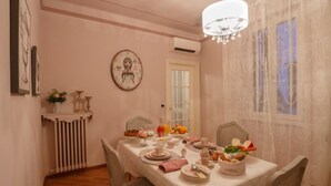 Een eetkamer met een tafel gedekt voor vier personen, met een witte tafelkleed, borden, kopjes en een middelpunt van fruit en bloemen.