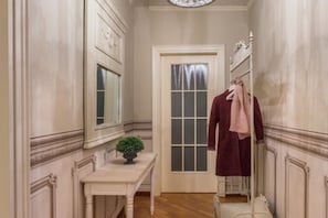 Un pasillo estrecho con una puerta blanca, una mesita con una planta y un perchero con una toalla rosa.
