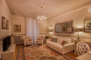 A traditional living room with a fireplace, a chandelier, a sofa, and a patterned rug.
