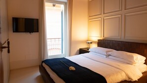 Ein Hotelzimmer mit Bett, Wandfernseher, Nachttisch mit Lampe und einem Fenster mit Vorhängen.