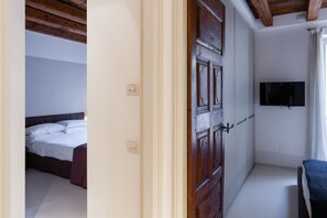 A bedroom with a wooden door, a bed, a TV mounted on the wall, and a small seating area. - A magnificent residence overlooking Piazza Erbe (Verona)