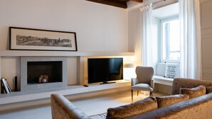 Ein Wohnzimmer mit Kamin, Fernseher, einer Couch und einem Fenster mit Vorhängen.