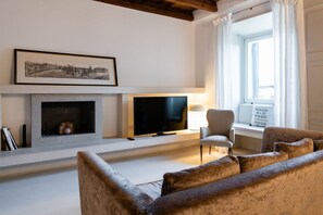 A living room with a fireplace, a television, a sofa, and a window with curtains. - Magnificent Residence overlooking Piazza Erbe (Verona)