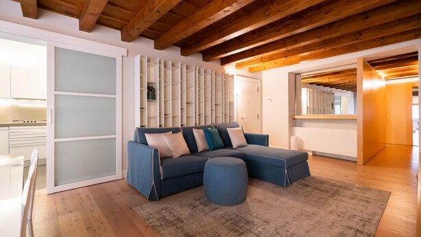 A modern living room with a sectional sofa, a round ottoman, and a wooden ceiling. -  Modern Apartment 50 meters from Piazza Erbe (Verona)