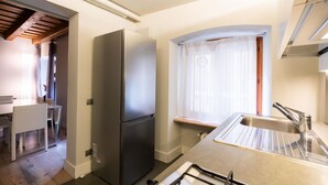 Een kleine keuken met een geïntegreerde koelkast, een spoelbak en een eethoek met stoelen.