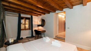 A bedroom with a wooden ceiling, a bed with white linens, a desk with a chair, and a mirror on the wall. -  Modern Apartment 50 meters from Piazza Erbe (Verona)