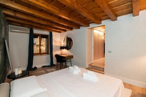 Een slaapkamer met een houten plafond, een bed met witte lakens, een bureau met stoel en een spiegel aan de muur.