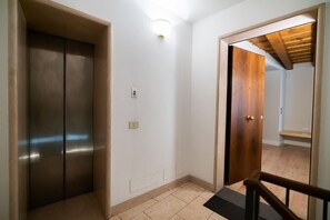 Un pasillo con un ascensor metálico, una puerta de madera y una lámpara en la pared.