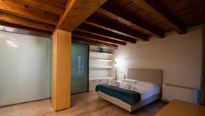 Een slaapkamer met een houten plafond, een bed met een wit hoofdeinde, een nachtkastje en een bijzettafeltje.