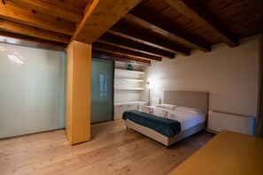 Une chambre avec un plafond en bois, un lit doté d’une tête de lit blanche, une table de chevet et une commode.