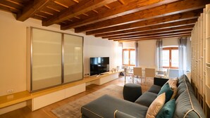 A modern living room with a wooden ceiling, a large sliding glass door, a flat-screen TV, a sofa, and a dining area with a table and chairs. -  Modern Apartment 50 meters from Piazza Erbe (Verona)
