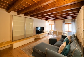 Een moderne woonkamer met een houten plafond, een grote schuifdeur, een flatscreen televisie, een bank en een eethoek met een tafel en stoelen.
