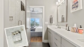 Ein modernes Badezimmer mit Dusche, Waschtisch und einem Bett, das durch eine offene Tür sichtbar ist.