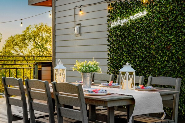 An outdoor dining area with a table set for four, surrounded by chairs, a potted plant, and lanterns.
