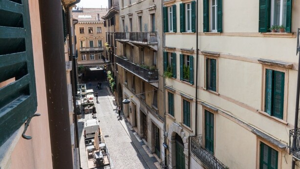 A narrow street with buildings on both sides, featuring balconies and windows with shutters. - Cozy Residence Rocchetto - 25 meters from P. Erbe (Verona)