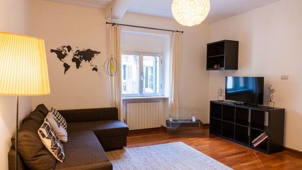 A modern living room with a sofa, a TV on a black stand, a world map on the wall, and a large window with curtains. - Cozy Residence Rocchetto - 25 meters from P. Erbe (Verona)