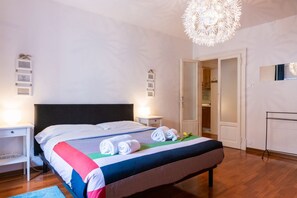 A neatly made bed with rolled towels, a bedside table, a nightstand, a hanging light fixture, and a wardrobe. - Cozy Residence Rocchetto - 25 meters from P. Erbe (Verona)