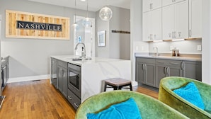 Cozinha moderna com uma placa de madeira com a inscrição "WELCOME TO NASHVILLE", uma ilha central e uma área de jantar com cadeiras verdes.