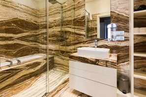 A bathroom with a marble wall, a glass shower enclosure, a white sink, and a mirror.