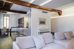 Una sala de estar moderna con sofá y piano, una zona de cocina con taburetes de bar, y un comedor con mesa y sillas.