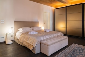 Un dormitorio moderno con una cama grande, lámparas de noche, un banco y una alfombra tradicional.